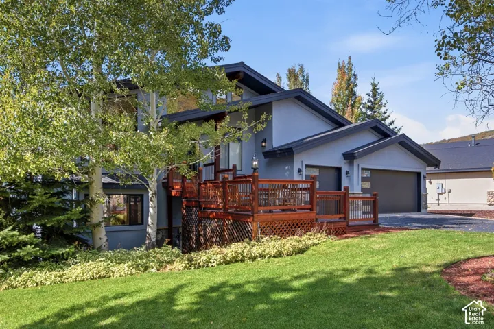 Multi-level exterior featuring a wood-tone deck, attached multi-car garage, and stone masonry foundation accents