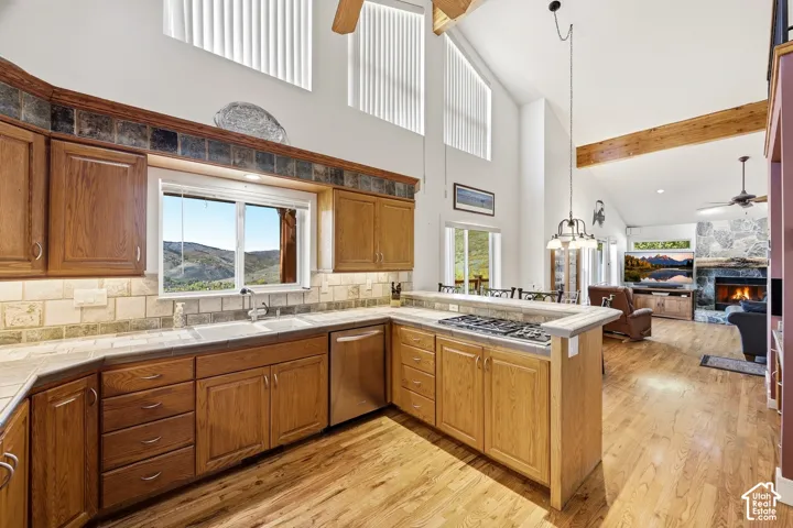 Kitchen featuring oak cabinetry, tile countertops and backsplash, wood-finish flooring, vaulted ceilings, and natural stone fireplace surround