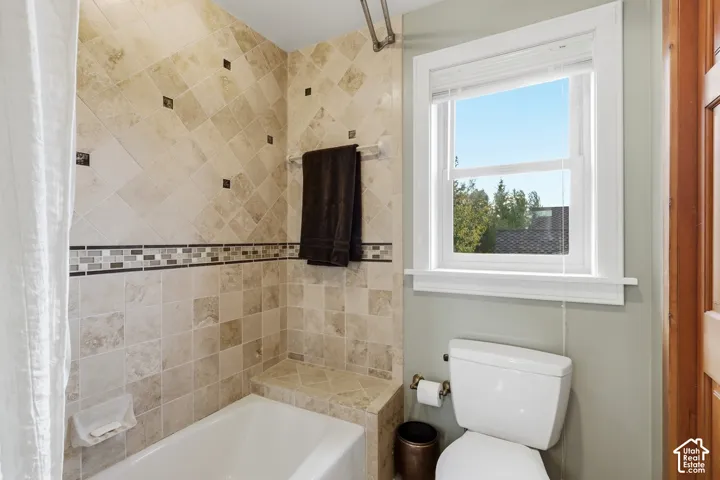 Bathroom featuring a tub surround with diamond-pattern stone tiling, decorative glass tile inlay, an integrated stone ledge, and a single-hung window with white casing