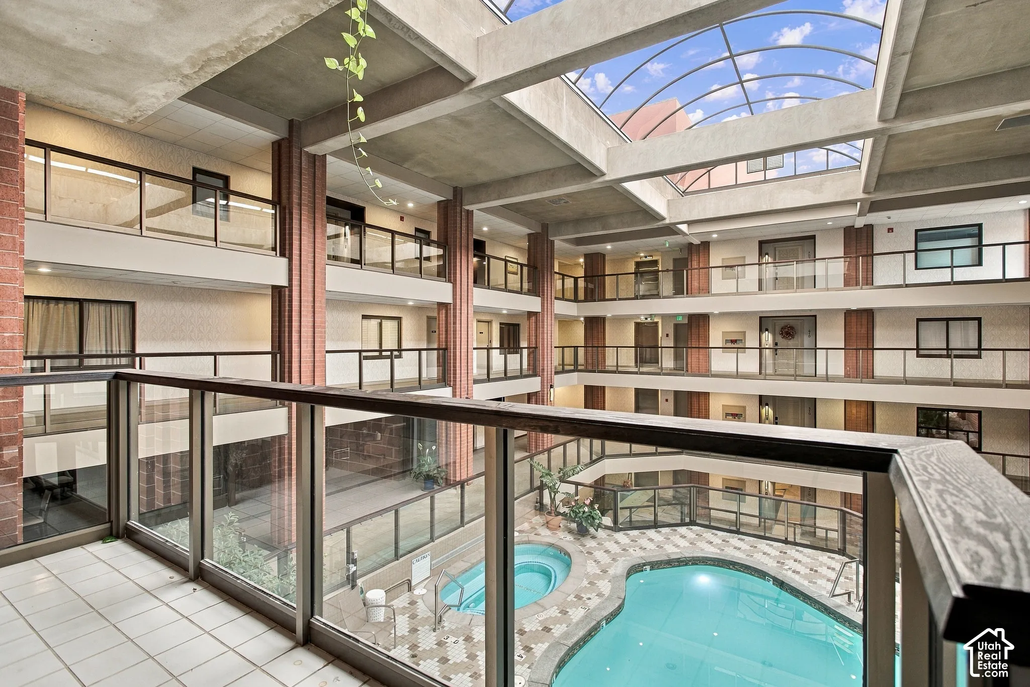 Atrium featuring a retractable skylight, multi-level glass-railed corridors, concrete structural columns, and a central swimming pool with integrated spa