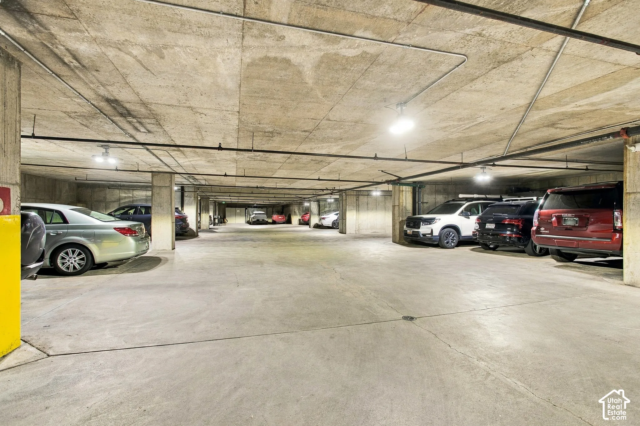 Covered parking garage featuring exposed concrete ceiling, support pillars, and overhead industrial lighting