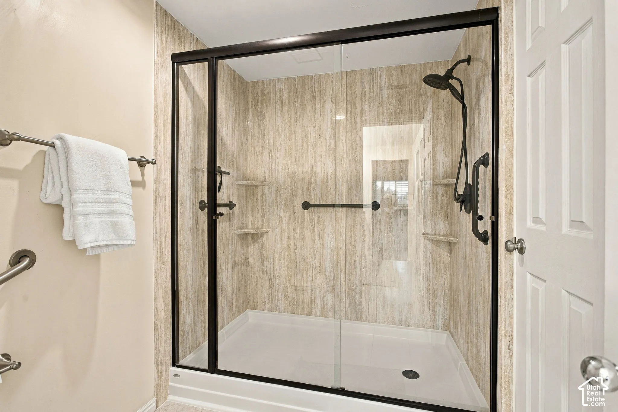 Walk-in shower featuring glass enclosure with matte black framing, textured wall surround, built-in shelving, and adjustable handheld shower head