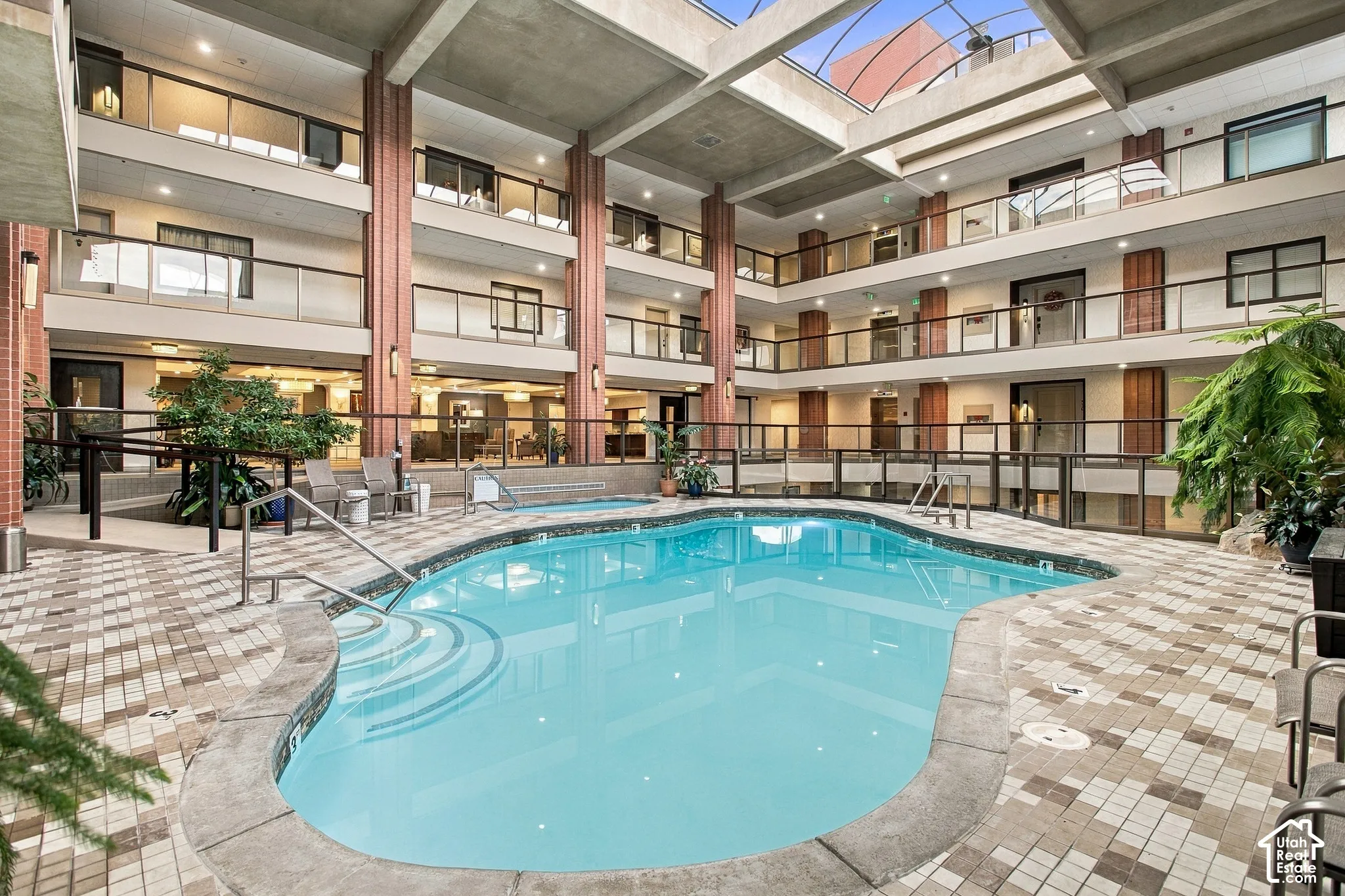 Atrium featuring a retractable skylight, an in-ground swimming pool, multi-level balconies with glass railings, concrete structural columns, and patterned stone tile decking