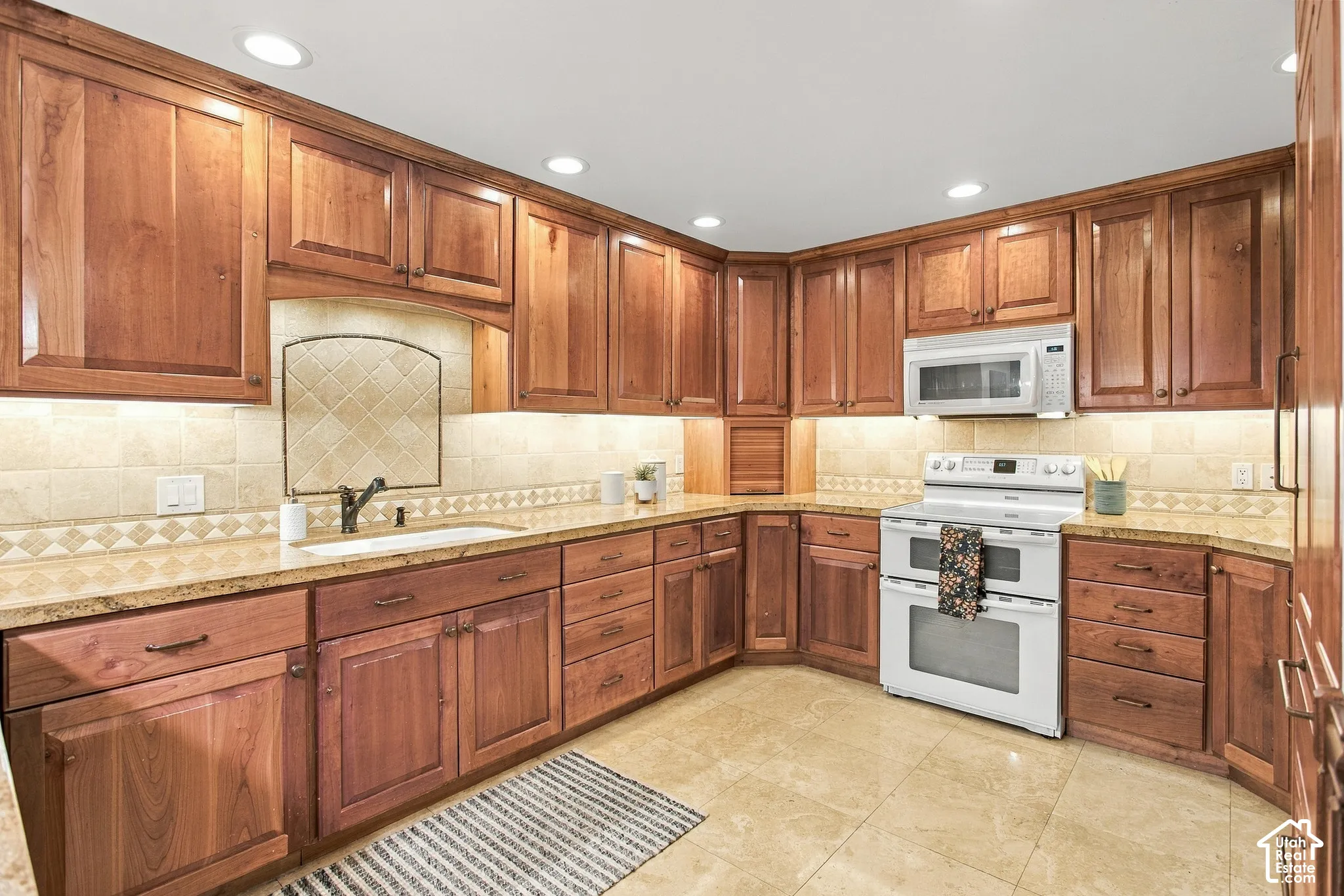 Kitchen featuring stained wood cabinetry, stone countertops, stone tile backsplash, recessed lighting, and tile flooring