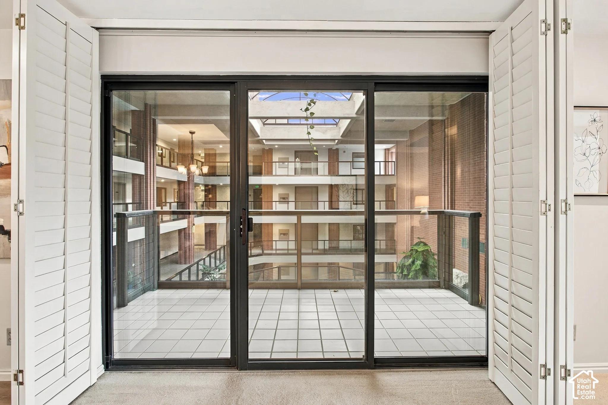 Floor-to-ceiling sliding glass door system framed by white plantation shutters, featuring a tiled balcony with metal railing