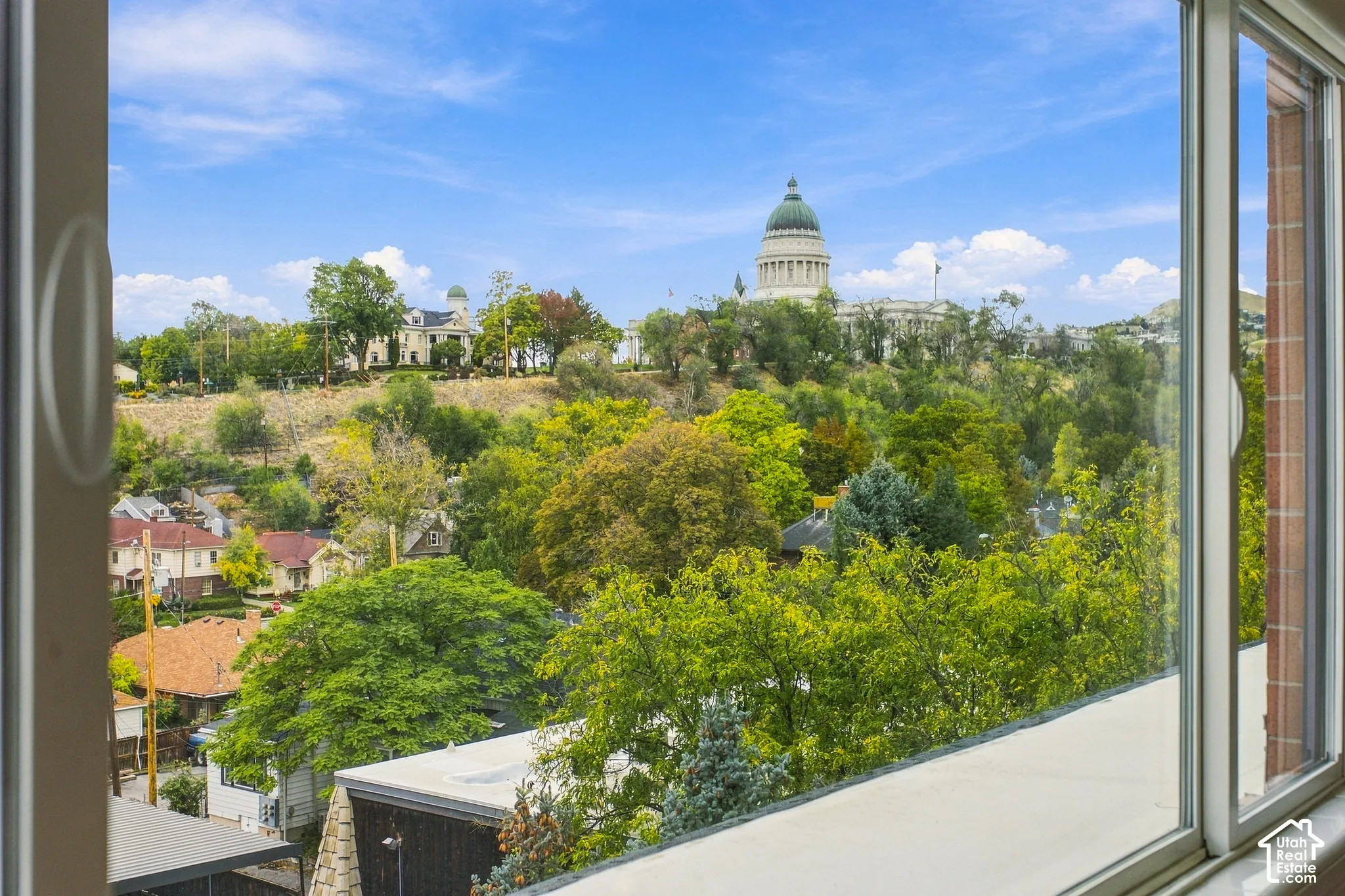 Expansive sightline featuring the state capitol building, mature trees, and urban surroundings, framed by a large multi-pane window