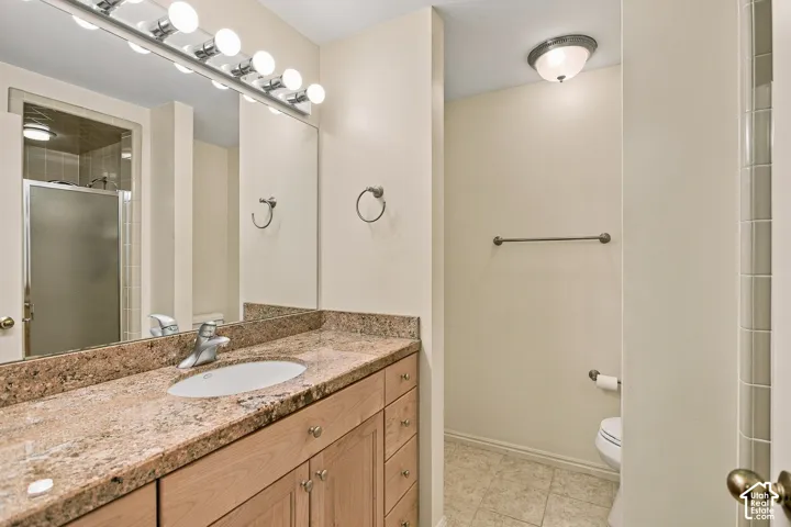 Bathroom featuring a wood vanity with stone-finish countertop, undermount sink, multi-bulb overhead lighting, and full-width mirror