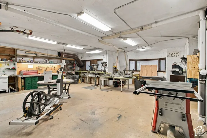 Expansive workshop area featuring concrete flooring, integrated industrial lighting, built-in wooden shelving, and multi-paned windows