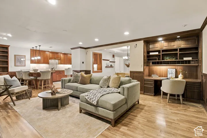 Open-concept living space featuring wood-finish flooring, custom built-in dark wood cabinetry with integrated desk workspace, recessed lighting, and wooden wainscoting
