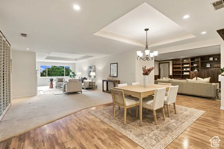 Open-concept living space featuring wood-finish flooring, recessed lighting, double tray ceilings, a multi-arm chandelier, and floor-to-ceiling built-in cabinetry