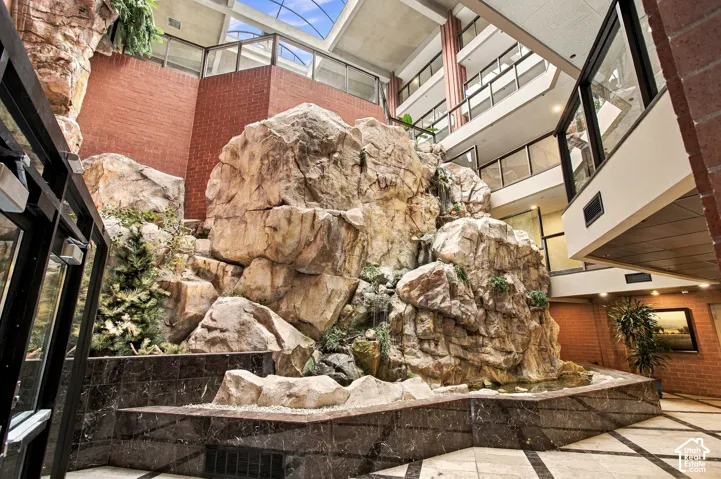 Atrium featuring a multi-story natural stone rock formation with integrated water feature, skylight ceiling, red brick masonry walls, and stone-tiled flooring