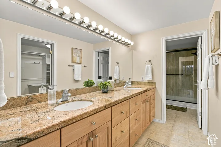 Dual-sink vanity with natural stone countertop, full-width wall mirror, wood cabinetry, and integrated vanity lighting