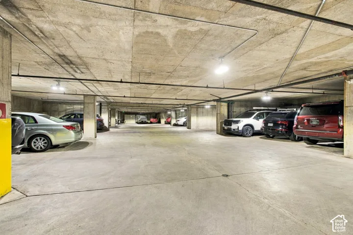 Covered parking garage featuring exposed concrete ceiling, support pillars, and overhead industrial lighting