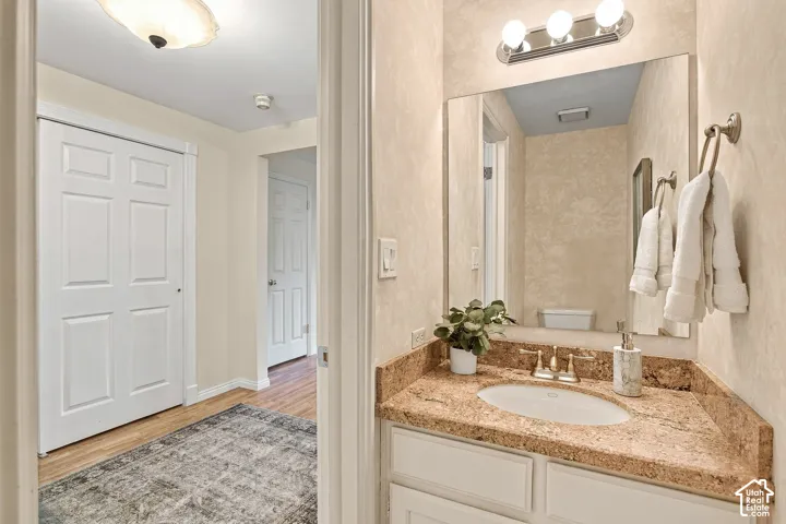 Bathroom featuring a vanity with a stone countertop, oval undermount sink, multi-light fixture, large wall-mounted mirror, and white shaker-style cabinetry