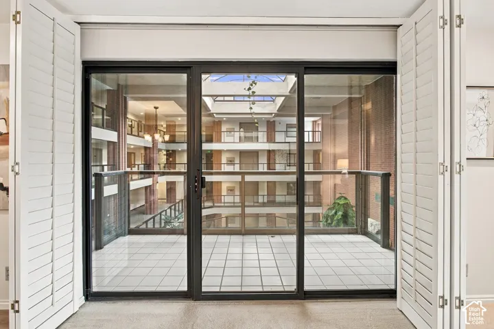 Floor-to-ceiling sliding glass door system framed by white plantation shutters, featuring a tiled balcony with metal railing