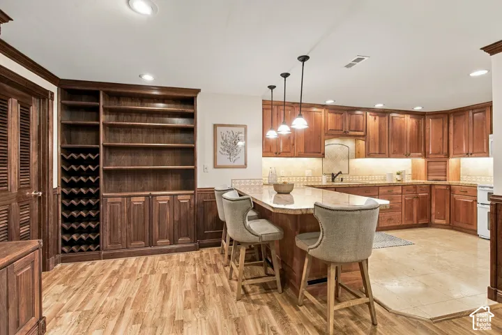 Kitchen featuring custom wood cabinetry, stone countertops, built-in wine storage, recessed lighting, and a kitchen island with pendant fixtures