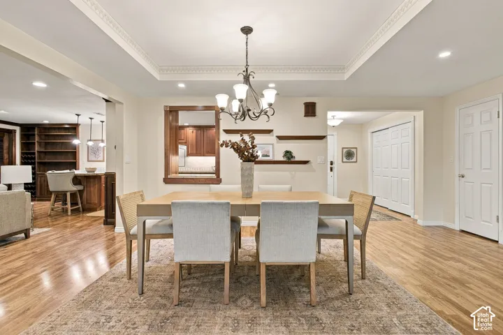 Dining area featuring a tray ceiling with crown molding, wood-finish flooring, a tiered metal chandelier, recessed lighting, and wall-mounted wooden display shelves