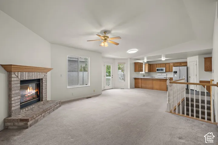 Brick fireplace with wood mantel, vaulted ceilings, ceiling fan, kitchen cabinetry with built-in appliances, and staircase with wooden handrail