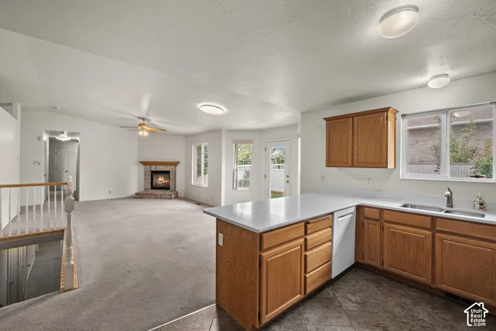 Kitchen featuring wood cabinetry, solid-surface countertops, and tiled flooring, accompanied by a living area with carpeting and a brick fireplace