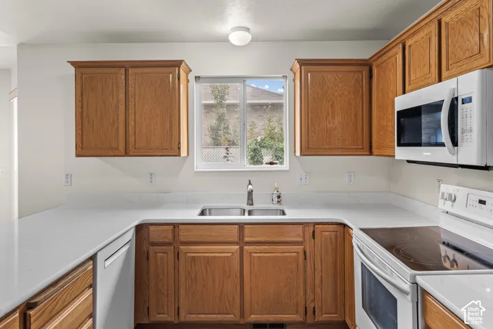 Kitchen featuring natural wood cabinetry, white stone-composite countertops, a dual-basin undermount sink, and white appliances
