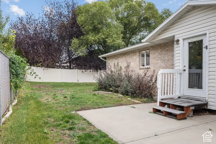 Exterior featuring a brick and vinyl siding facade, concrete patio, white vinyl perimeter fencing, and wood-framed exterior staircase