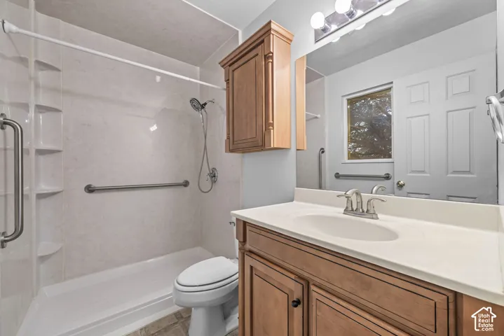 Bathroom featuring a wood-finish vanity with a molded countertop and sink, a built-in wooden wall cabinet, and a shower surround with integrated shelving and wall-mounted grab bars