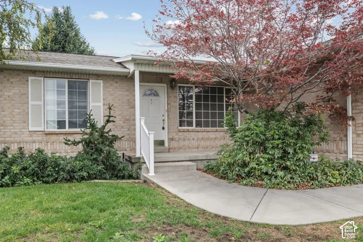 Single-story brick exterior featuring a covered front porch, concrete walkway, multi-light windows with shutters, and mature landscaping