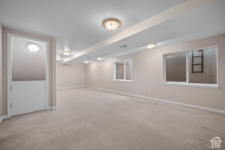 Open floor plan featuring wall-to-wall carpeting, recessed and flush-mount ceiling lighting, dual egress windows, and a privacy door with a textured glass upper panel