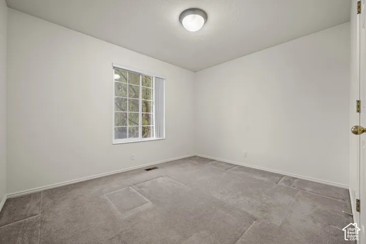 Neutral-toned carpeting, crisp white wall finish, window with divided lites, and a flush-mount ceiling light fixture
