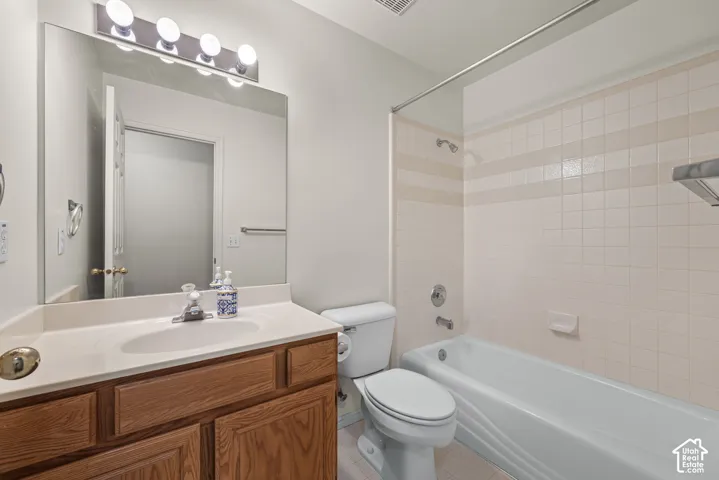Bathroom featuring a wood-tone vanity with a solid surface countertop, an integrated sink, full-width wall mirror, and a tub-shower combination with tiled surround