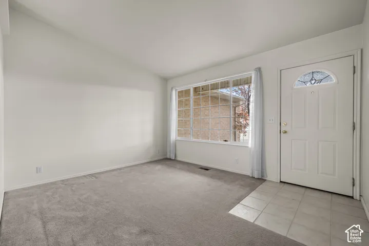 Entry area featuring neutral carpeting, ceramic tile flooring, vaulted ceilings, and a front door with a glass-paneled accent