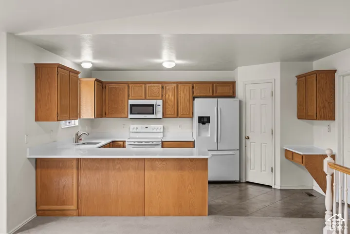 Kitchen featuring wood cabinetry, white solid-surface countertops, built-in white appliances, and tiled flooring