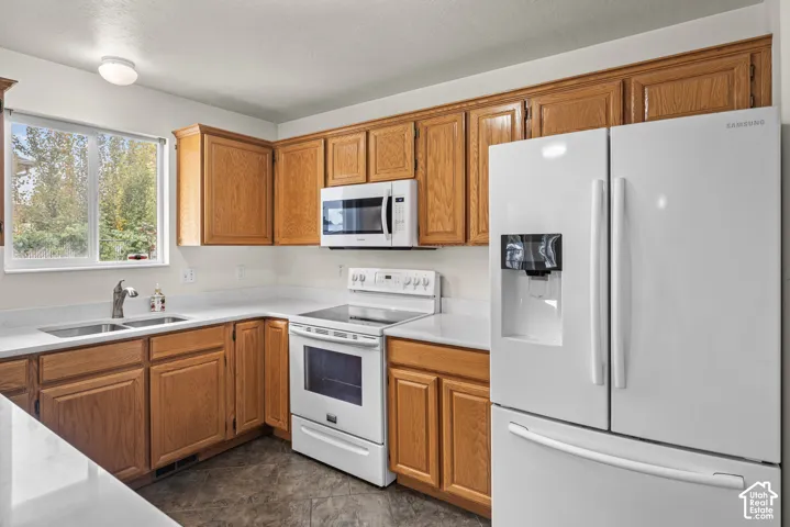 Kitchen featuring wood cabinetry, white countertops, double-basin sink, and white appliances including a built-in microwave and refrigerator