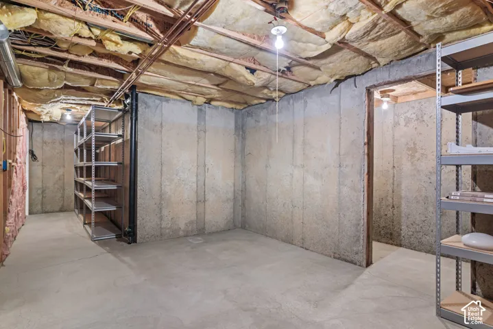 Unfinished lower-level space featuring poured concrete walls, concrete flooring, exposed joist ceiling with insulation, and pull-string pendant lighting