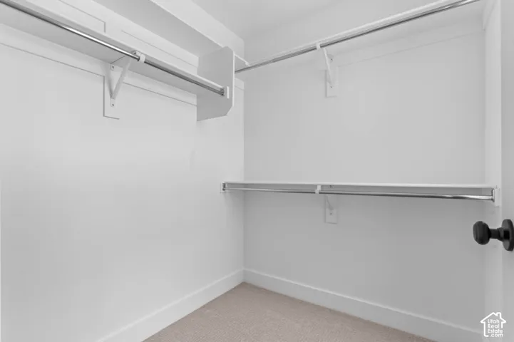 Walk-in closet featuring tiered metal garment rods, white built-in shelving, and neutral carpeting