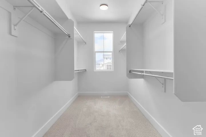 Walk-in closet featuring floor-to-ceiling shelving, dual-level metal hanging rods, wall-to-wall carpeting, and a central window