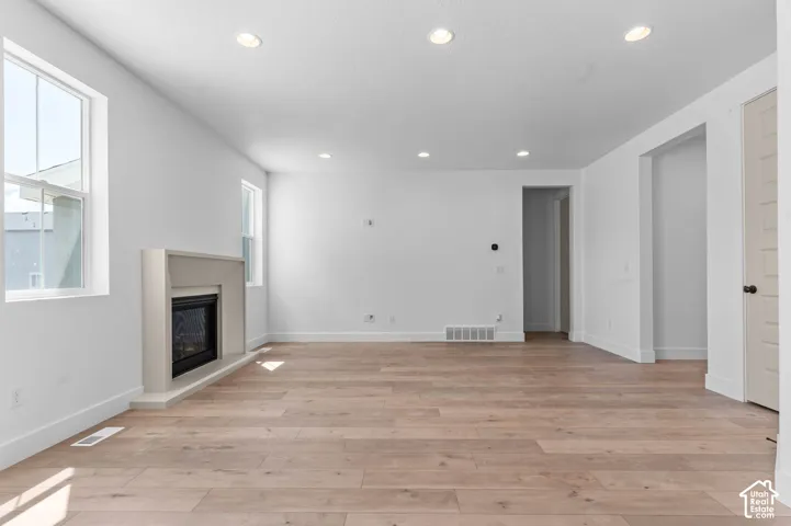 Open-concept interior featuring light wood-finish flooring, recessed lighting, and a built-in fireplace with a minimalist surround
