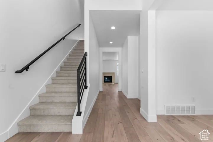 Staircase featuring a matte black metal railing, carpeted treads, wood-finish flooring, recessed lighting, and a fireplace in the distance