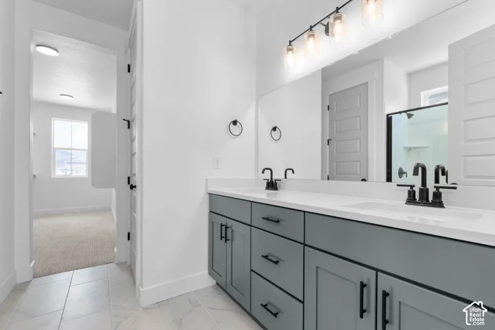 Double vanity with quartz countertop, dual under-mount sinks, matte black fixtures, grey cabinetry with shaker-style doors, and three-light vanity fixture