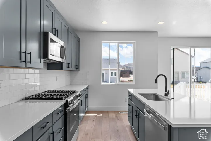 Kitchen featuring slate-grey shaker cabinetry, white stone countertops, a subway tile backsplash, stainless steel appliances, and wood-finish flooring