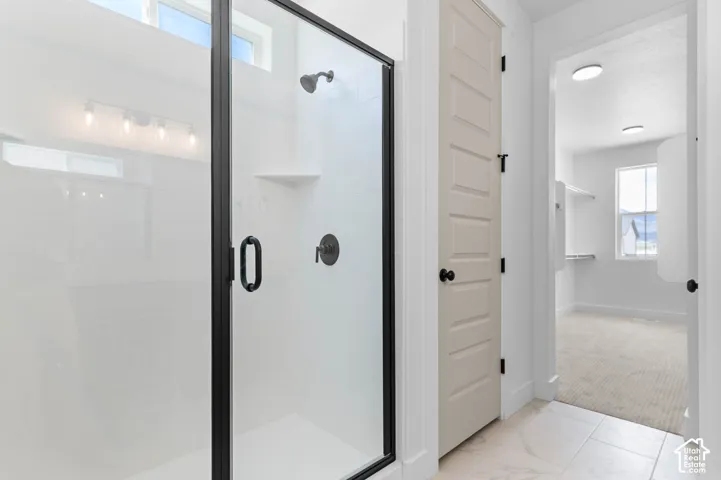 Shower featuring a glass enclosure with matte black hardware, built-in shelving, tile flooring, and a five-panel interior door
