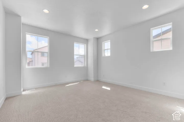 Neutral-toned carpeted flooring, four windows with natural lighting, and recessed ceiling lighting