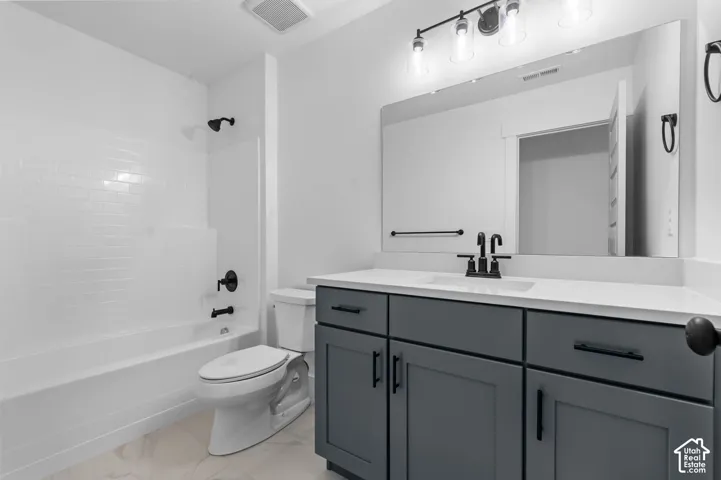 Bathroom featuring a gray shaker-style vanity with a light-toned countertop, integrated rectangular sink, matte black hardware, and an expansive wall-mounted mirror