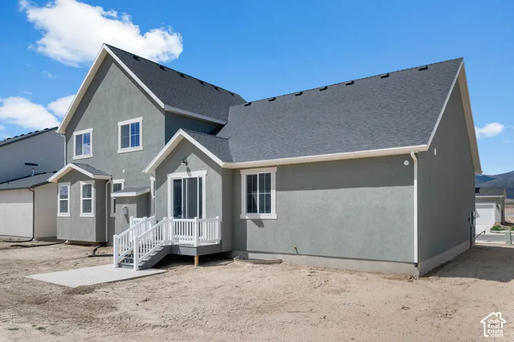 Two-story residence featuring a gray stucco exterior, dark asphalt shingle roof, white window trim, and a raised white vinyl deck with stairs leading to a concrete patio