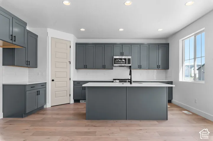 Kitchen featuring dark gray cabinetry, central island with a quartz countertop, white subway tile backsplash, stainless steel microwave, and wood-finish flooring