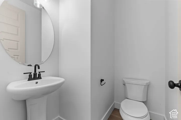 Pedestal sink with a matte black widespread faucet, large circular wall-mounted mirror, and wood-finish flooring