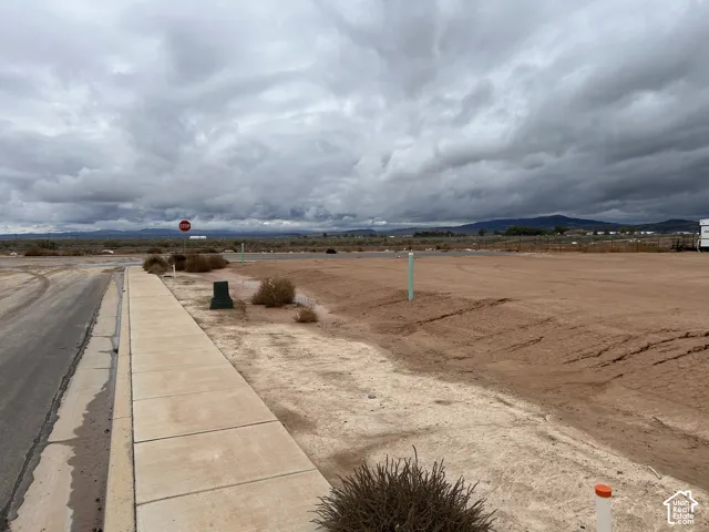 Vacant land parcel featuring paved street access, concrete sidewalk, utility connection points, and mountain terrain backdrop