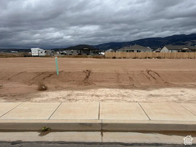 Vacant residential lot featuring concrete curbing, paved sidewalk, and mountain backdrop