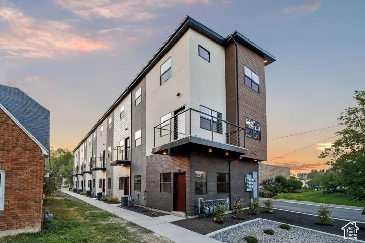 Contemporary multi-story exterior featuring a mixed-material facade of brick, wood-finish siding, and stucco, accented by metal-railed balconies