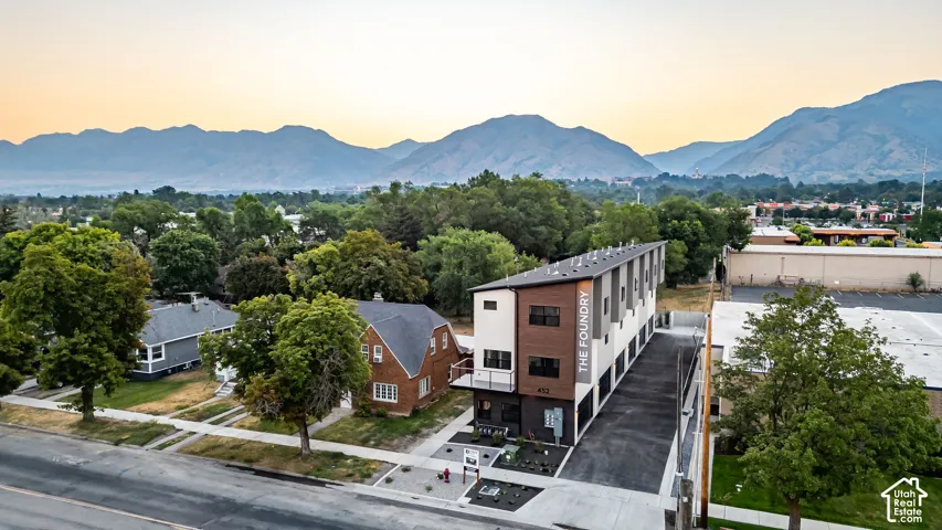Multi-story building featuring a contemporary facade with dark-toned brick, smooth stucco finishes, horizontal wood-style paneling, and an attached balcony set against a prominent mountain backdrop